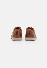 Scarpe in pelle marrone con una finitura liscia, con un retro arrotondato morbido, cuciture arancioni a contrasto e una leggera suola in gomma beige.