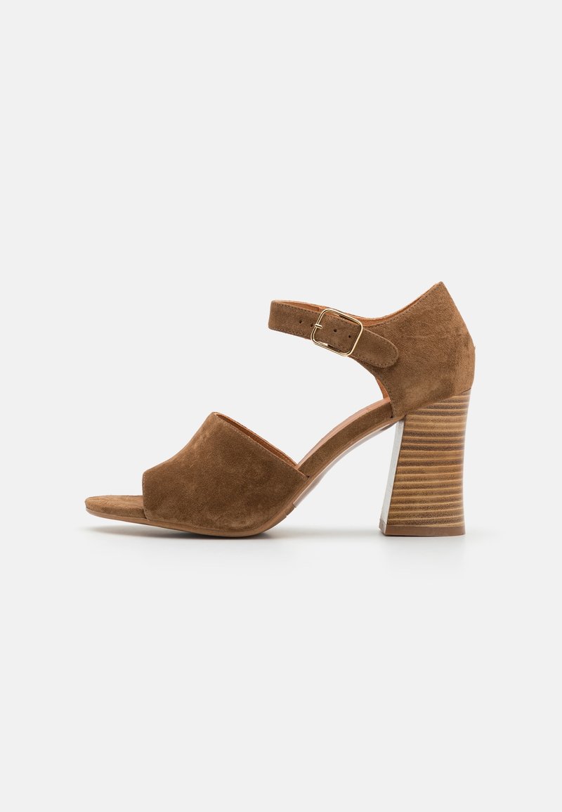 Sandale à talons hauts en daim marron, ouverte sur l'avant, avec une bride à la cheville et un talon bloc strié. Texture lisse, design classique et couleur neutre.