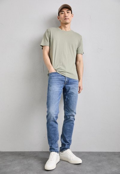 T-shirt en coton vert olive, jeans en denim bleu clair et baskets blanches. Look simple et décontracté avec un col rond et des manches courtes.