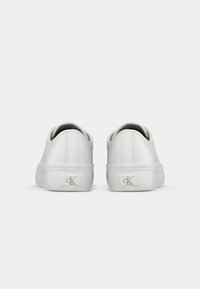Weiße Sneakers im Low-Top-Stil von hinten betrachtet, mit dem "cK"-Logo an der Ferse beider Schuhe vor einem schlichten weißen Hintergrund.