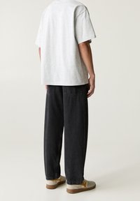 Camiseta de algodón gris con mangas cortas, corte holgado, combinada con pantalones de mezclilla negros. El calzado es de color gris claro con acentos amarillos y suelas marrones.