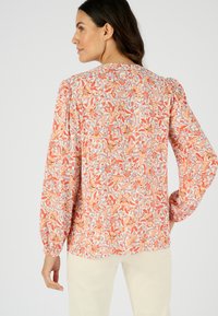 Langemouwenblouse van lichte stof met een levendig bloemmotief in oranje, blauw en beige tinten en met voluminieuze schouderinzetten.