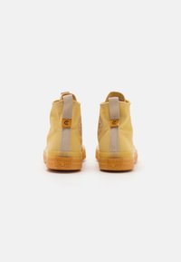 Bottines en toile jaune avec des accents beige, patch logo à l'arrière et semelle en caoutchouc transparent. Dotées d'une languette pour un enfilage facile.