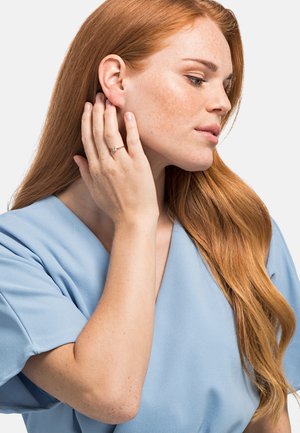 Blusa blu con maniche larghe, indossata da una persona con lunghi capelli rossi. Anello notevole con una pietra rotonda sulla mano vicino al viso.