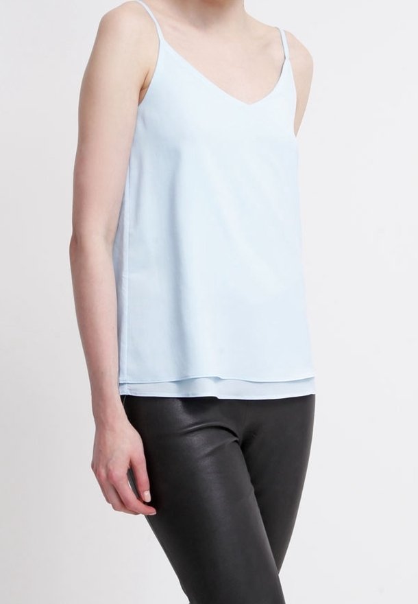 Top de tirantes azul claro con escote en V, tirantes finos y una textura suave, combinado con pantalones de cuero negros. Diseño simple y minimalista.