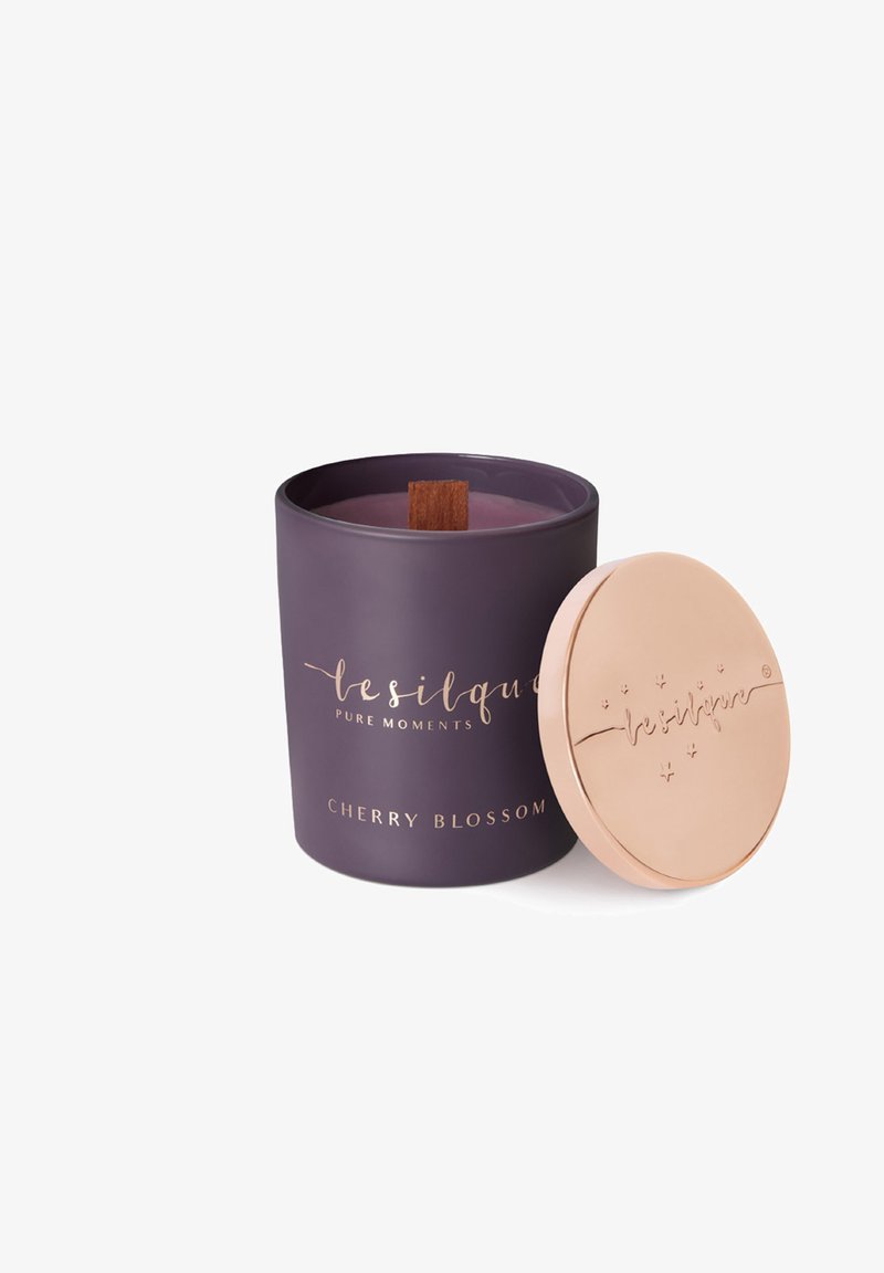 Lila Kirschblüten-Duftkerze mit Holzdocht in einem Behälter, neben einem runden beigen Deckel mit erhabenem Text.