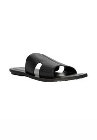 Black leather slide sandal with wide textured straps and open toe, featuring a flat sole and minimalist design.