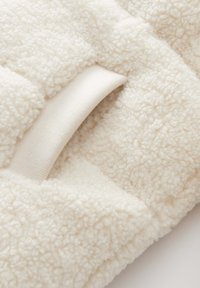 Coperta in pile color crema con una superficie morbida e un texture dettagliata, dotata di anelli in tessuto per una facile maneggevolezza.
