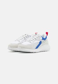 Adidași albi cu accente albastre și roșii, design din materiale mixte cu plasă și piele întoarsă, vârf rotunjit și talpă din cauciuc texturat.