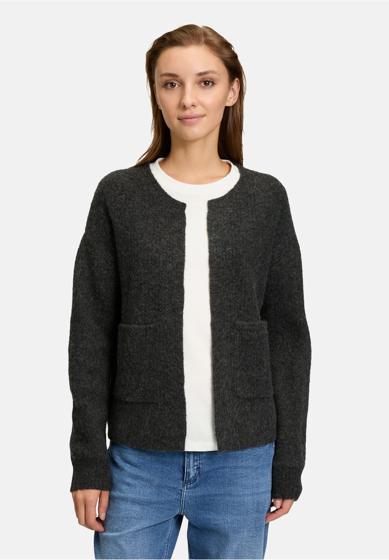 Ciemnoszary kardigan wykonany z teksturowanej wełny, z długimi rękawami, dwoma przednimi kieszeniami i okrągłym dekoltem. Nosi się go na białej bluzce.