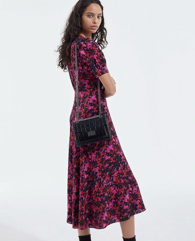 Abito nero a fiori con maniche corte, caratterizzato da fiori rosa e rossi, dalla silhouette svasata, abbinato a una borsa nera trapuntata e stivali alla caviglia.