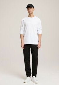 Biała koszulka z długim rękawem, czarne dresowe spodnie, czapka w kolorze czarnym i białe sneakersy, stojąca na neutralnym tle. Prosty wzór i luźny krój.