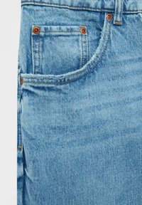 Ljusblå denimjeans med en framficka med kopparnitar, synlig sömnad och en lätt bleknad textur.