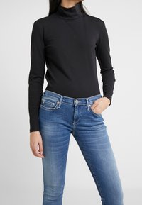Maglione nero a collo alto con maniche lunghe, realizzato in tessuto morbido. Abbinato a jeans slim-fit azzurri chiari con bottone e cinque tasche.