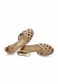 Sandalias desnudas con tiras que presentan un diseño trenzado, un tacón bajo y una correa en el tobillo. La plantilla muestra el nombre de la marca en letras doradas.