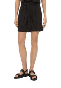 Shorts en lin noirs avec une taille à nouer, à coupe décontractée et avec des poches latérales. Associés à des sandales noires à tresses.