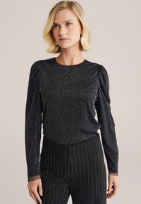 Top nero a maniche lunghe con una texture scintillante e spalle arricciate, abbinato a pantaloni neri a righe sottili.