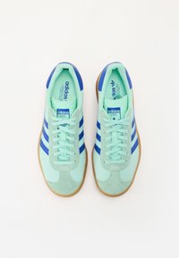 Ljusgröna Adidas sneakers med blå detaljer, suède och syntetiska material, med tre blå ränder, runda snörningar och en gummisula.