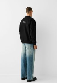 Svart sweatshirt med rund hals, enfärgad baksida och vit textdetalj. Tillsammans med vida ljusblå jeans och svarta skor.