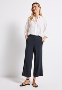 White button-up shirt with long sleeves, paired with navy wide-leg pants and black strappy sandals. Smooth fabric and relaxed fit.