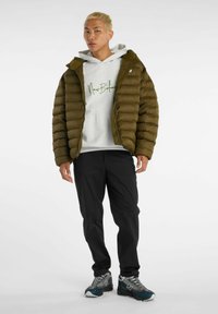 Puffy olive green jacket with a hood, worn over a grey hoodie featuring green text. Black pants and grey and blue sneakers complete the look.