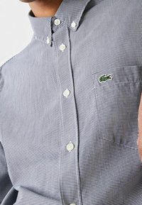 Mustavalkoruudullinen napillinen paita kauluksella, jossa on valkoiset napit ja rintataskussa vihreä kirjailtu logo.