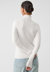 Light gray turtleneck sweater with long sleeves, ribbed hem and cuffs, showcasing a soft, smooth texture. Worn with jeans.