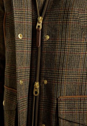 Brown checked jacket made of textured fabric featuring a gold zipper, brown leather accents, and brass snap buttons.