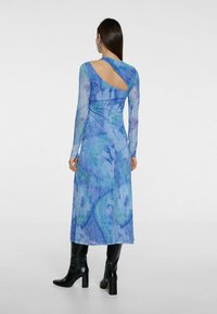 Langärmliges, blaues Gradienten-Kleid mit abstrakten Mustern, Rückenausschnitt, fließender Stoff, geschichtetes Design, getragen mit schwarzen kniehohen Stiefeln.