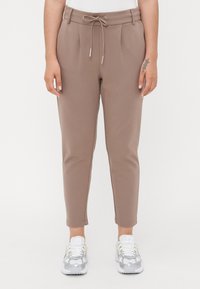 Pantalons marron ajustés avec une taille à cordon de serrage, des plis à l’avant, coupe slim et longueur cheville. Assortis avec des chaussures de sport argentées.