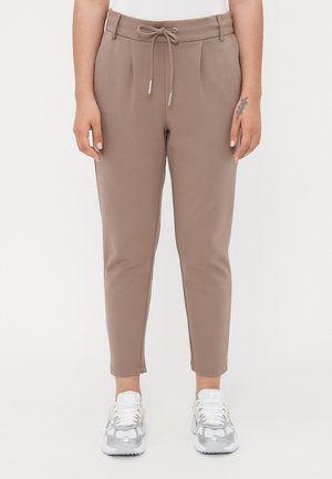 Brune tilpassede bukser med snor i livet, forpleats, smal passform og anklelengde. Kombinert med sølvfargede joggesko.