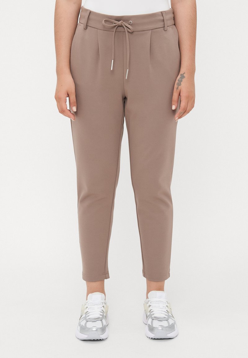 Brune tilpassede bukser med snor i livet, forpleats, smal passform og anklelengde. Kombinert med sølvfargede joggesko.