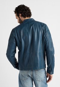 Blauwe leren jas met ribbelaccenten op de schouders en textuurpanelen aan de zijkanten, voorzien van een staande kraag en een gladde afwerking.