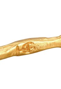 Kuldtoon metallist tööriist, millel on tekstureeritud orgaaniline kuju, millel on graveeritud logo ja märgised, mis näitavad hõbedasisaldust.