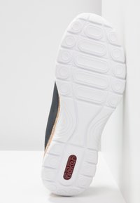 Chaussure noire avec une semelle en caoutchouc blanc texturé ornée de motifs circulaires et d'un accent logo rouge, mettant en avant un design épuré et une finition lisse.