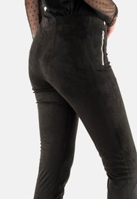 Pantalones de ante sintético negro con un diseño ajustado, textura suave, bolsillos laterales con cremallera y detalles de costura mínimos.