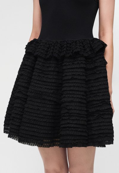Robe noire avec un corsage ajusté et une jupe évasée faite de volants horizontaux superposés.