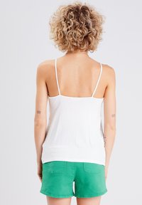 Haut blanc à bretelles spaghetti avec des panneaux latéraux texturés, associé à un short vert. Le haut a une coupe ample et un tissu lisse.