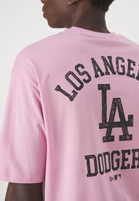 Camiseta de algodón rosa con letras negras desgastadas que dicen "LOS ÁNGELES" y "DODGERS" con un destacado logo de "LA" en la parte de atrás.