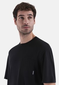 Black short-sleeve t-shirt made of soft fabric with a chest pocket and a side tag. Simple design with a crew neckline and relaxed fit.