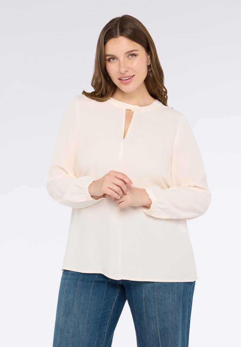 Blusa color pesca chiaro con scollo rotondo, dettaglio a chiave e maniche lunghe elasticizzate, abbinata a pantaloni in denim a righe blu.