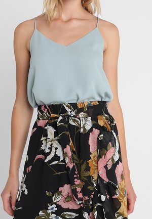 Woman wearing a light blue sleeveless blouse tucked into a high-waisted black floral skirt with a tied waist belt.