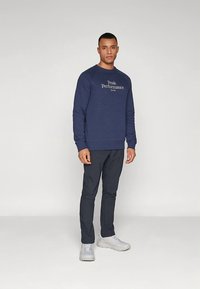 Námornícka mikina s logom "Peak Performance", s okrúhlym výstrihom a rebrovanými manžetami. Kombinovaná s tmavými nohavicami a svetlými športovými topánkami.