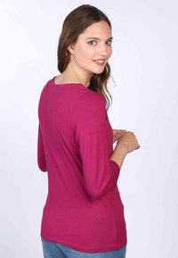 Fuchsia Langarm-Oberteil mit rundem Ausschnitt, das über eine glatte Textur und eine taillierte Passform verfügt, kombiniert mit blauen Jeans.