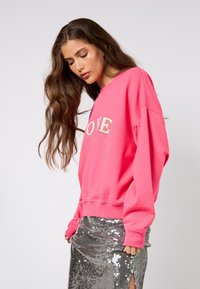 Fuchsiová mikina se zlatým nápisem "LOVE". Volný střih, kulatý výstřih, žebrované manžety, doplněná lesklou stříbrnou sukní posázenou flitry.