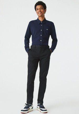Marineblauwe overhemden met lange mouwen en knoopsluiting, zwarte broek en sneakers in meerdere kleuren; met logo op het shirt. Gladde stof, op maat gemaakte pasvorm.