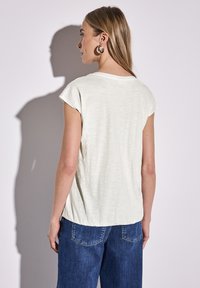 T-shirt a maniche corte di color verde chiaro con una vestibilità rilassata, caratterizzato da un orlo leggermente curvato e un tessuto morbido e strutturato. Indossato con jeans di denim blu.