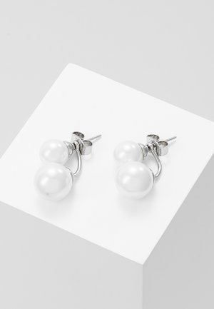 Boucles d'oreilles clous en argent avec deux perles blanches rondes de tailles différentes sur chaque, exposées sur une surface blanche inclinée.