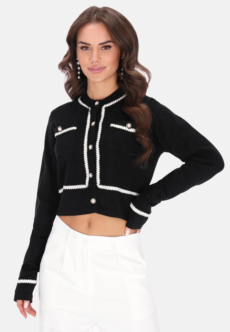 Fekete, rövidített kabát struktúrált anyagból, fehér díszítéssel, két mellzsebbel és nagyméretű gombokkal. Fehér nadrággal viselve.