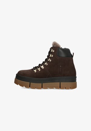 Bottines en daim marron avec des accents en cuir noir, œillets en métal doré et une semelle en caoutchouc épaisse et texturée. Doublure pelucheuse sur le dessus.
